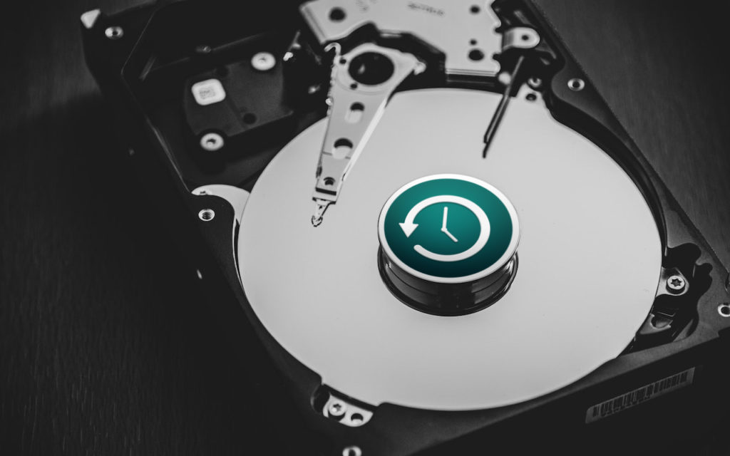A black and white photo of an open hard disk drive with a green backup or restore icon displayed on the central disk platter.