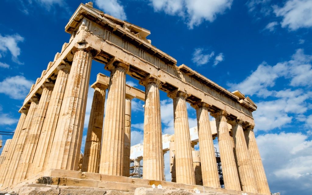 The Parthenon, an ancient Greek temple with tall stone columns and a partially ruined roof, stands under a bright blue sky with scattered white clouds.