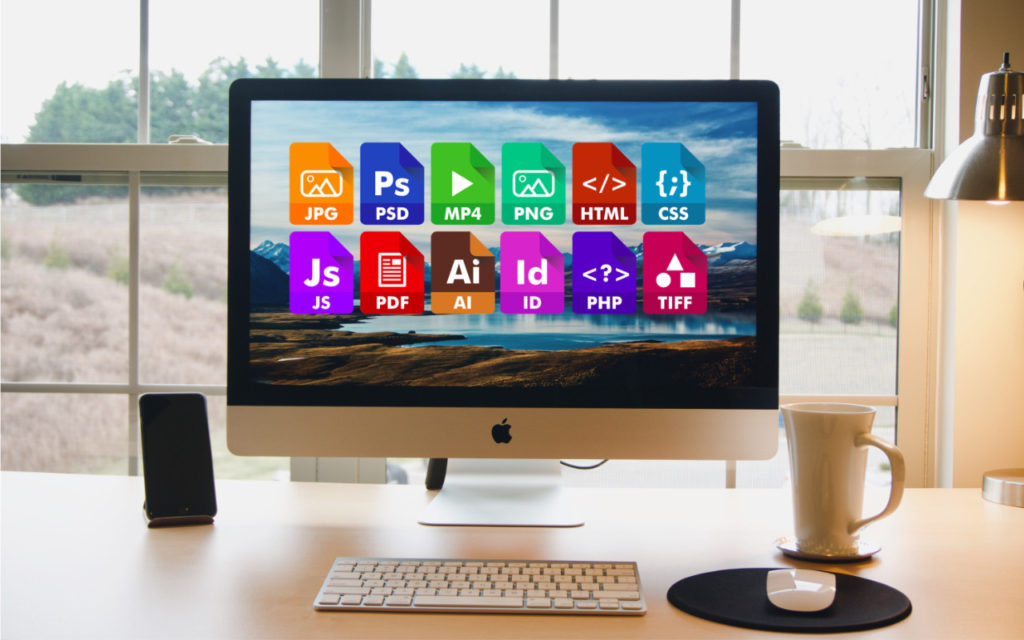 A desktop computer on a tidy desk displays colorful icons of various file formats and programs, including JPG, PSD, MP4, PNG, HTML, CSS, JS, PDF, AI, ID, PHP, and TIFF, against a scenic background.