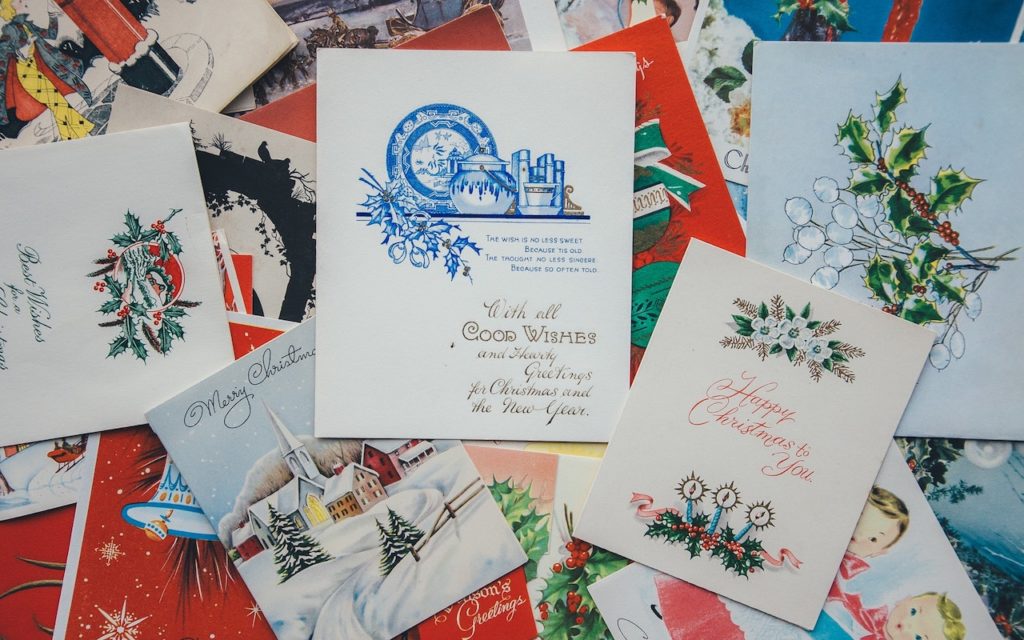 A collection of vintage Christmas cards with various festive designs, including holly, snowy scenes, and holiday greetings, arranged in a scattered, overlapping display.