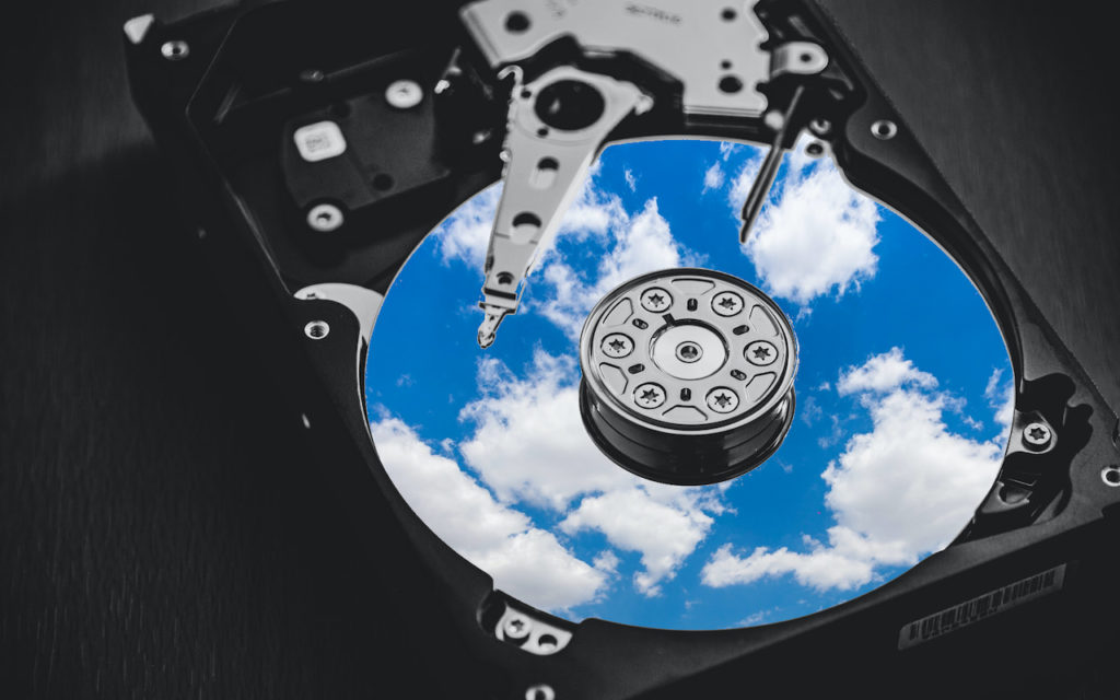 Close-up of an open hard drive, with the platter reflecting a bright blue sky and white clouds, symbolizing the concept of cloud storage or data in the cloud.