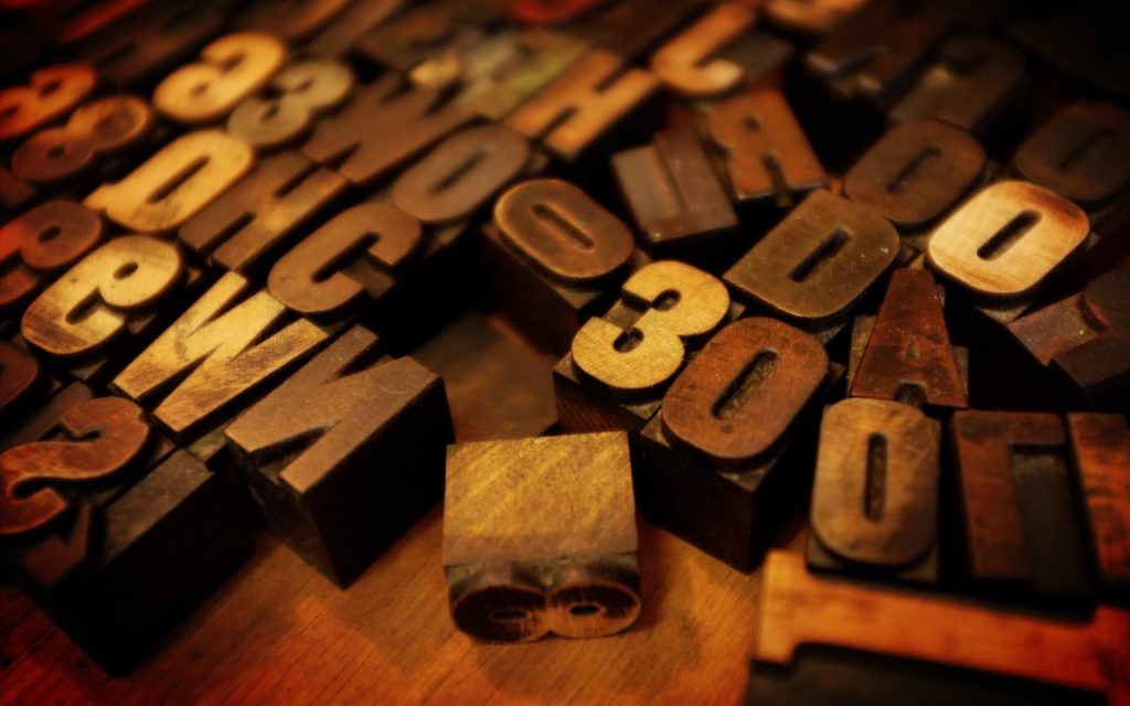 A collection of vintage wooden letterpress printing blocks, featuring various letters and numbers in different sizes and fonts, scattered on a wooden surface.