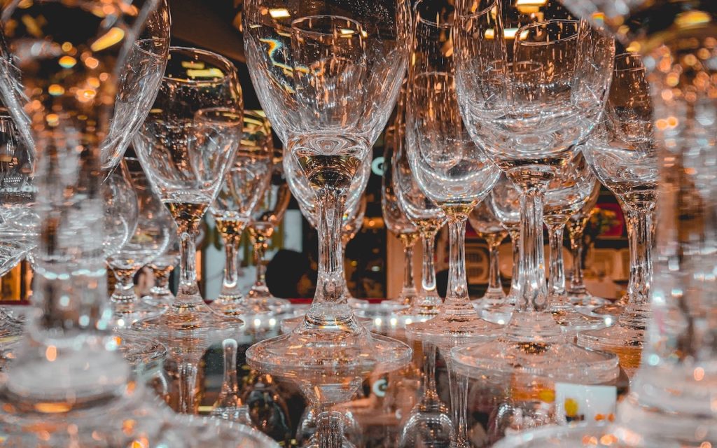 Close-up view of multiple empty wine glasses arranged upside down, creating reflections and patterns with warm, ambient lighting in the background.