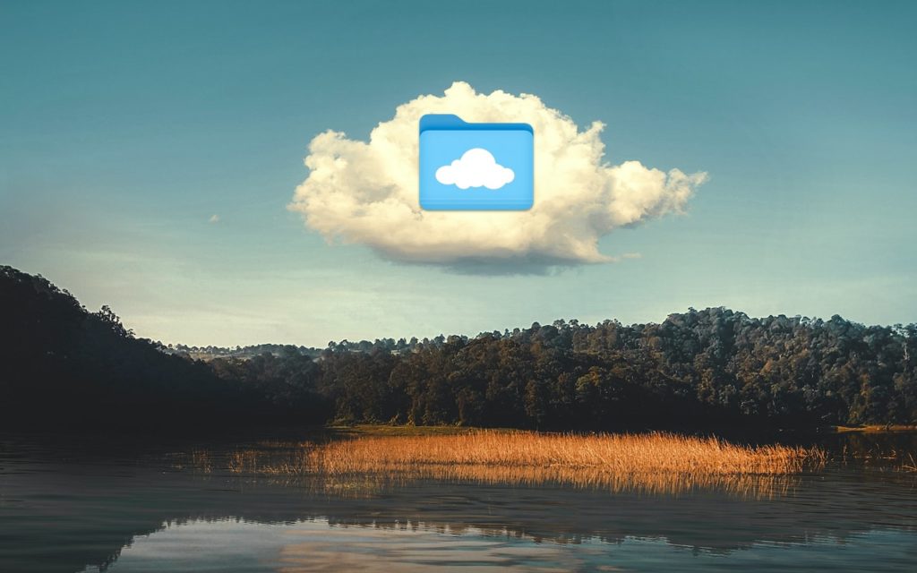 A fluffy white cloud floats over a lake and forested hills, with a blue computer folder icon featuring a cloud symbol superimposed on the cloud in the sky.