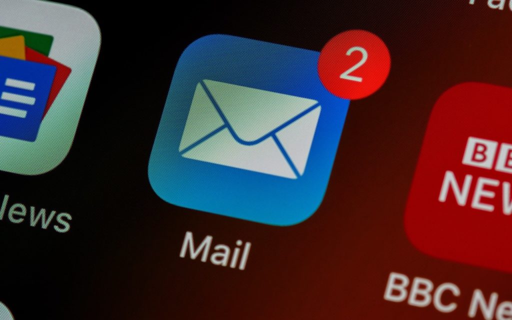 A close-up of a smartphone screen showing the Mail app icon with a red notification badge displaying the number 2, indicating two unread emails. Other app icons are partially visible nearby.
