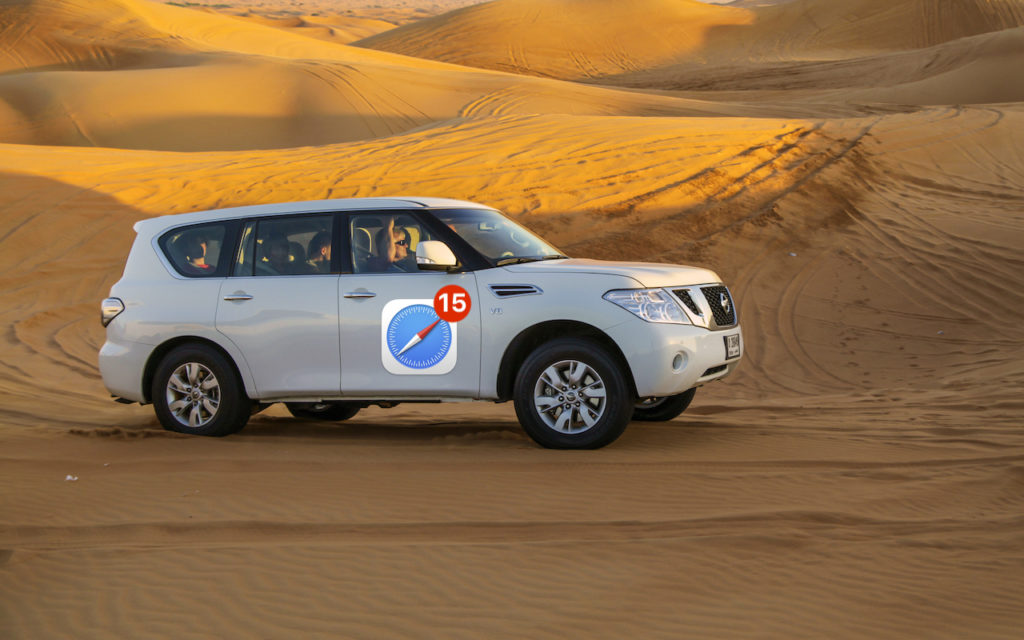 A white SUV with a large Safari browser icon and number 15 sticker drives across sandy desert dunes under a bright, golden sky.