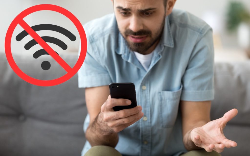 A man looks frustrated while holding his smartphone, with a large no Wi-Fi symbol overlaid, indicating a lack of internet connection.