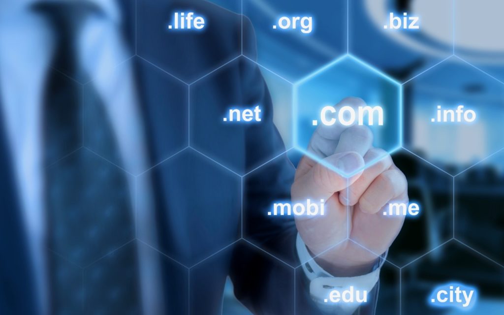 A person in a suit touches a virtual hexagonal button labeled .com on a digital screen, surrounded by other domain extensions like .net, .org, .edu, .biz, .info, .city, .mobi, .me, and .life.