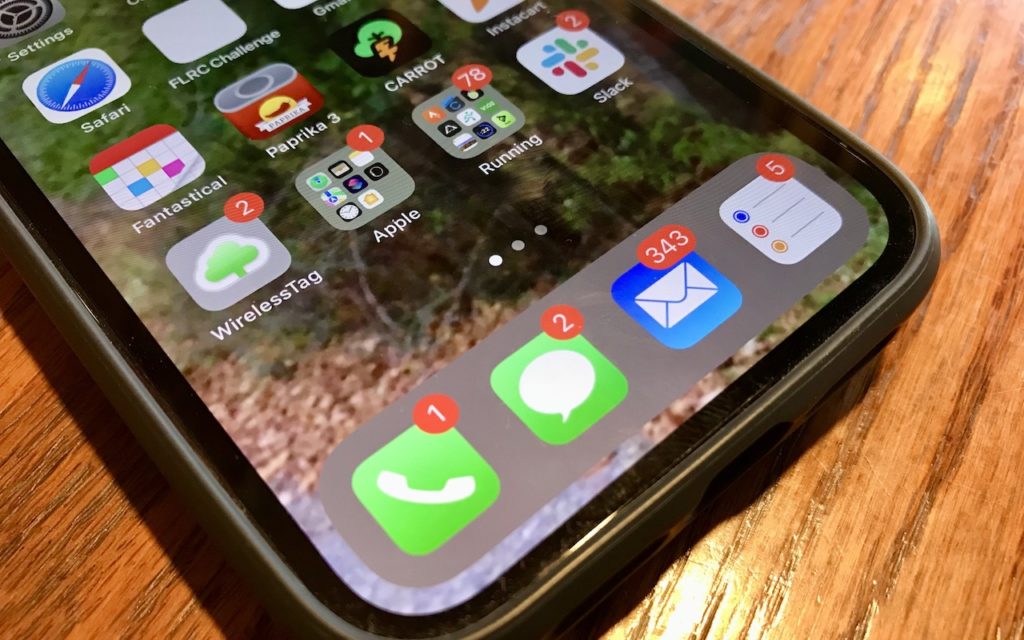 A smartphone displays its home screen, showing app icons with notification badges. The Mail app has 343 unread emails, Messages has 2, and Phone has 1. The phone rests on a wooden surface.