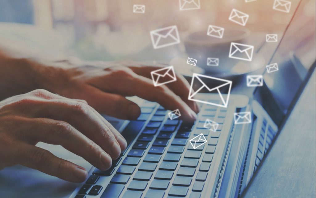 Hands typing on a laptop keyboard with illustrated email icons floating above, representing sending or receiving emails in a digital or online communication context.