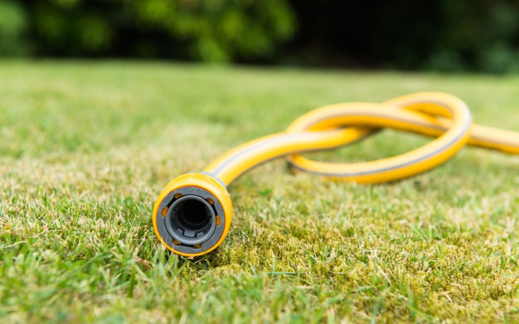A yellow garden hose lying on green grass, with the hose end in focus and the background blurred.