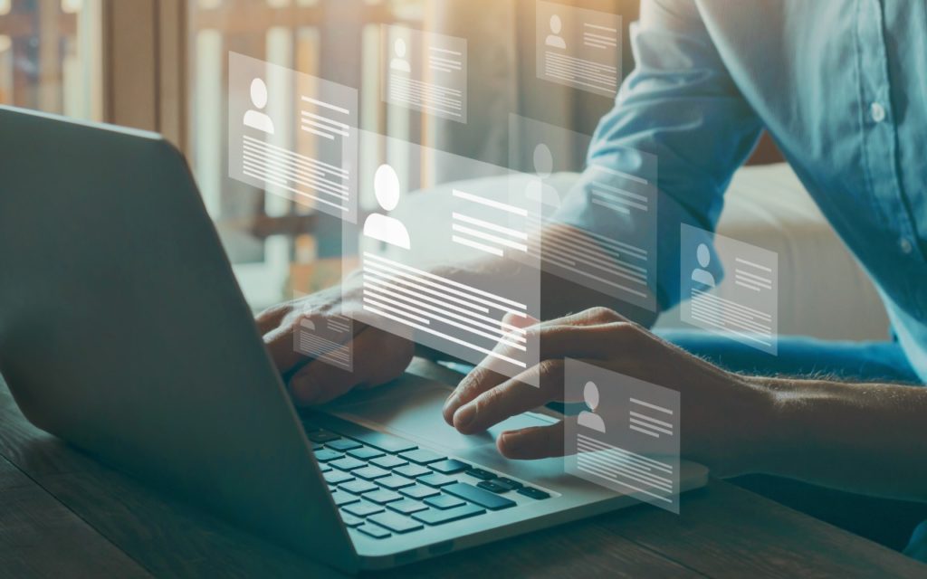 A person typing on a laptop with floating digital profile icons and information cards, representing online networking, data management, or digital communication in a modern setting.