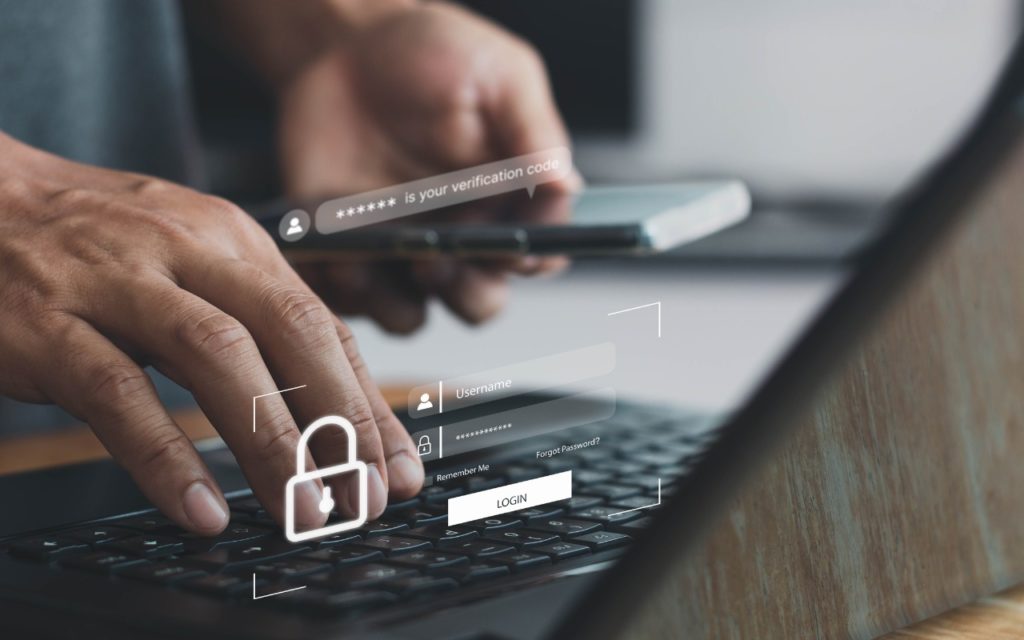 A person uses a smartphone and types on a laptop keyboard, with digital security icons and login fields overlaid, representing two-factor authentication and cybersecurity.