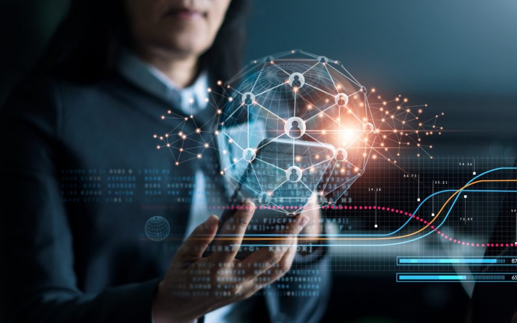 A person in a suit holds a glowing digital sphere with interconnected network icons and lines, representing global communication and technology, overlaid with data graphs and charts.