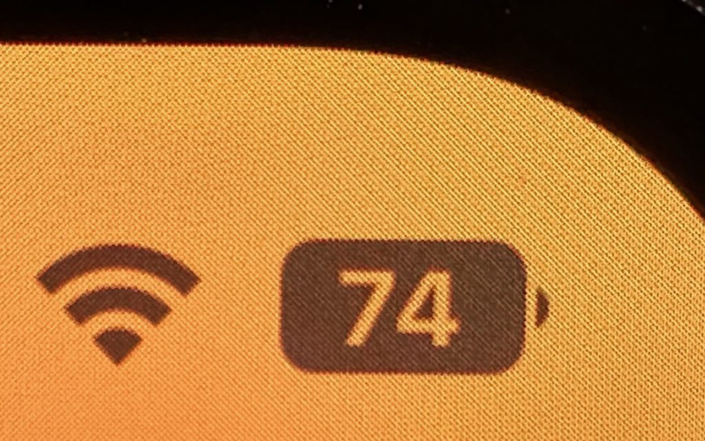 Close-up of a digital screen showing a Wi-Fi symbol and a battery icon displaying the number 74, indicating a 74% charge, on an orange-yellow background.