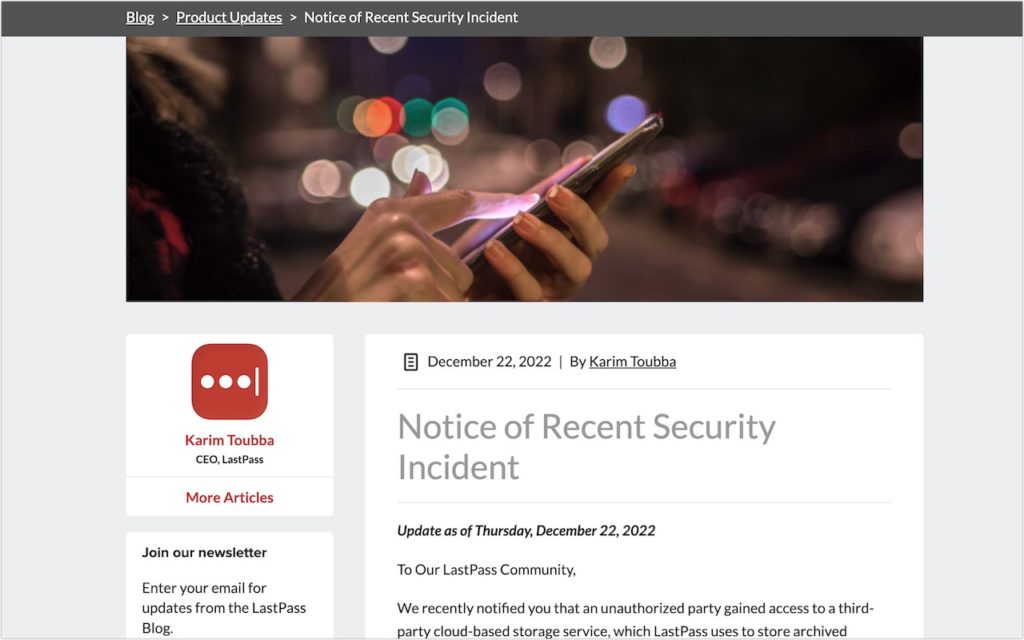 A person uses a smartphone at night with blurred city lights in the background. The foreground shows a webpage titled Notice of Recent Security Incident by LastPass CEO Karim Toubba.