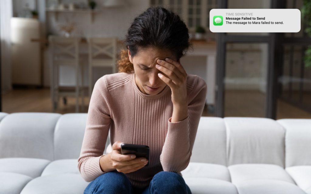 A woman sits on a couch holding her phone, looking stressed with her hand on her forehead. A notification on her phone reads, Message Failed to Send. The message to Mara failed to send.