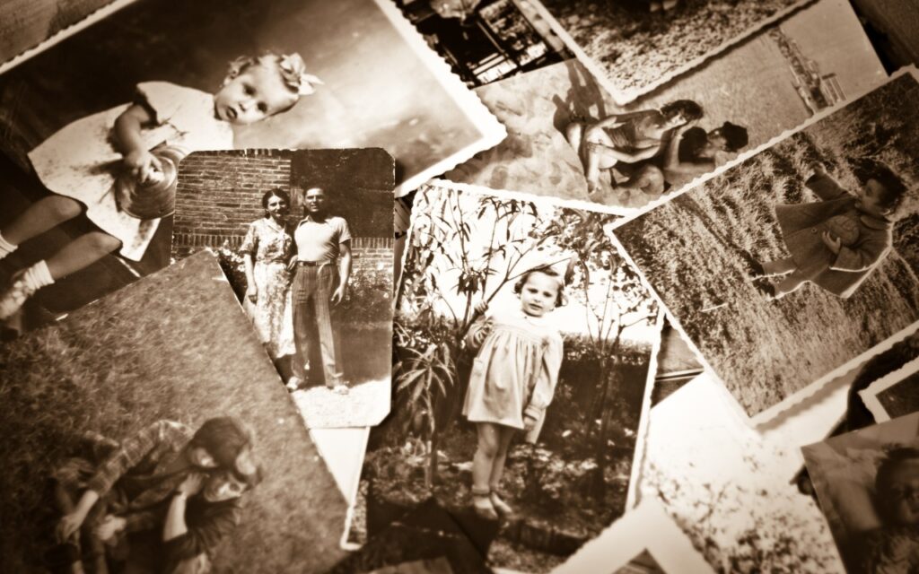 A sepia-toned collection of old, scattered photographs showing children, couples, and families posing outdoors and smiling, evoking memories of past generations and family history.