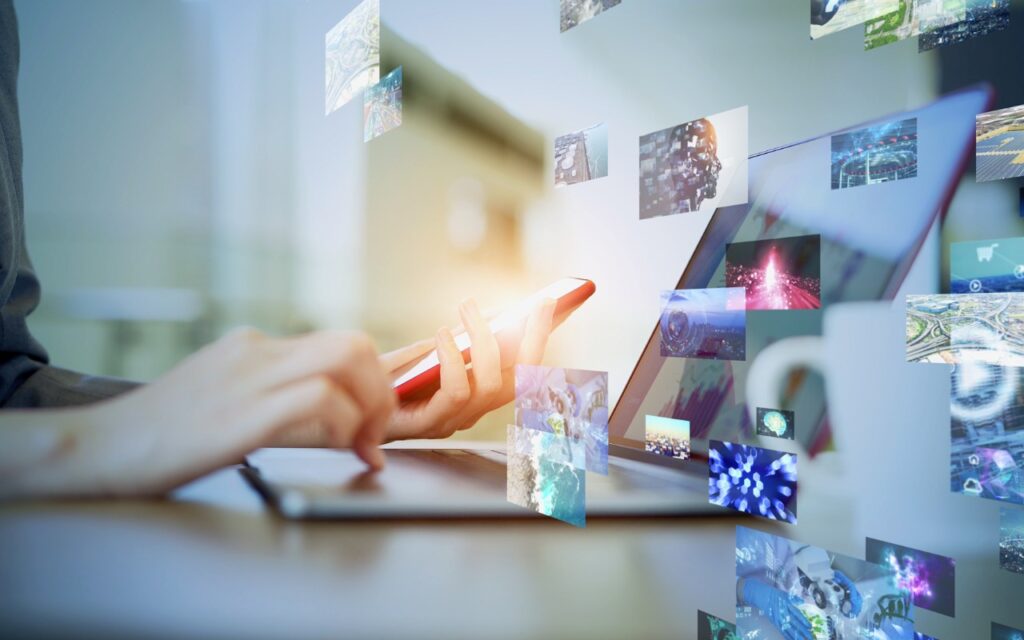 A person uses a smartphone and laptop, surrounded by floating digital images, representing multimedia, technology, and data sharing in a modern, connected workspace.