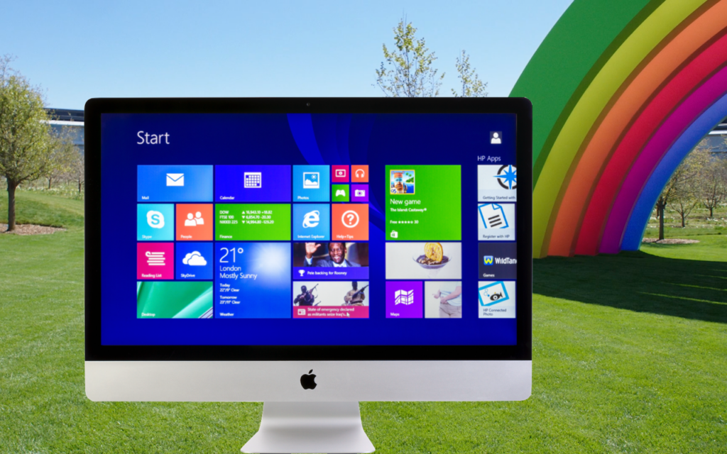 A desktop computer displaying the Windows 8 start screen stands outdoors on green grass, with colorful rainbow arches and trees in the background under a blue sky.