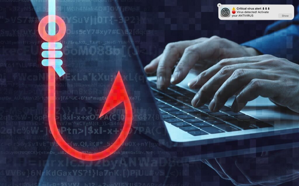 A person types on a laptop keyboard with a large red phishing hook and digital code overlayed. A “Critical virus alert” pop-up appears, warning of a detected virus and prompting antivirus activation.