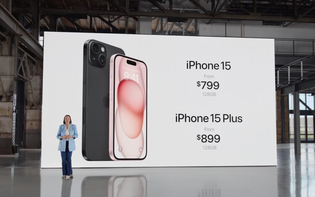 A presenter stands in front of a large screen displaying images of the iPhone 15 and iPhone 15 Plus, with prices starting at $799 and $899 respectively, both for the 128GB models.
