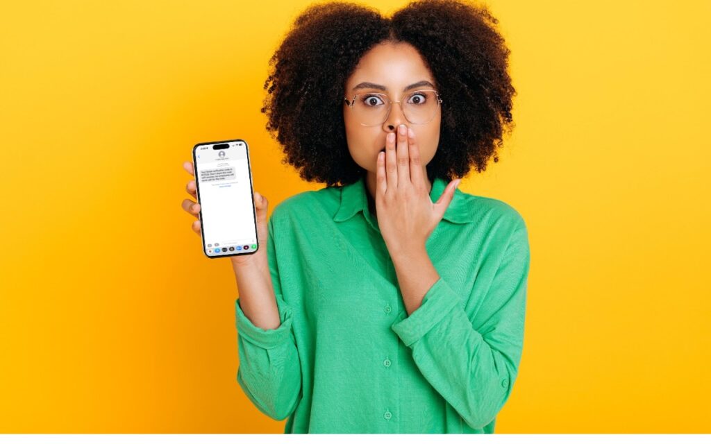 A surprised woman in a green shirt holds a smartphone displaying a message, covering her mouth with her other hand, standing in front of a bright yellow background.