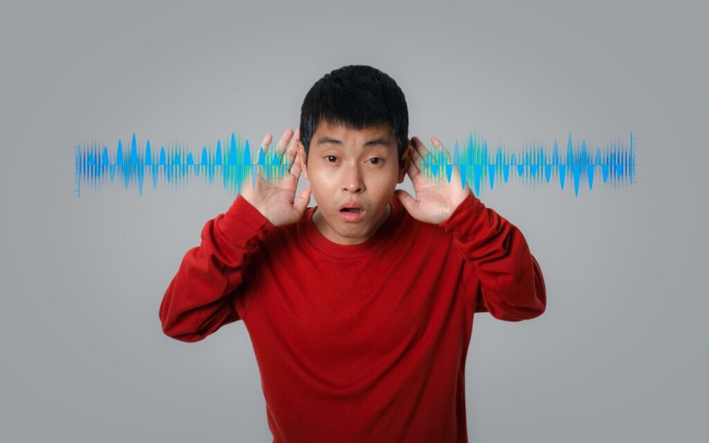 A surprised young person in a red shirt holds their hands to their ears, with colorful sound waves in the background—perfect for illustrating how to avoid head-tracked spatial audio for FaceTime audio calls.