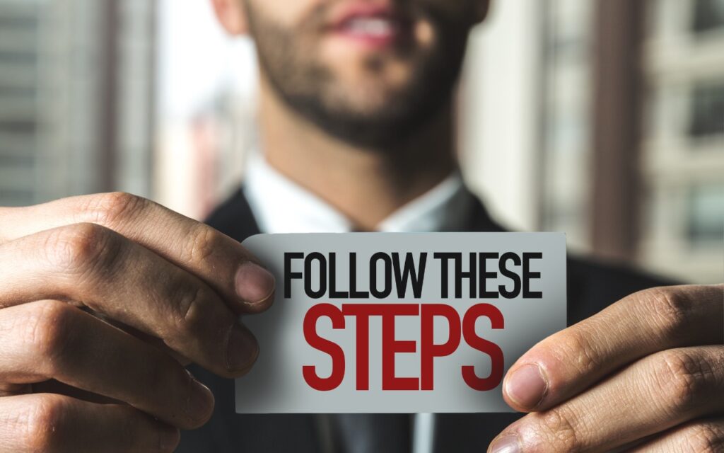 A man in a suit holds a card with the text FOLLOW THESE STEPS in bold black and red letters. Looking for Apple Manuals? Check the New Documentation Site, as the blurred background draws attention to the card and his hands.