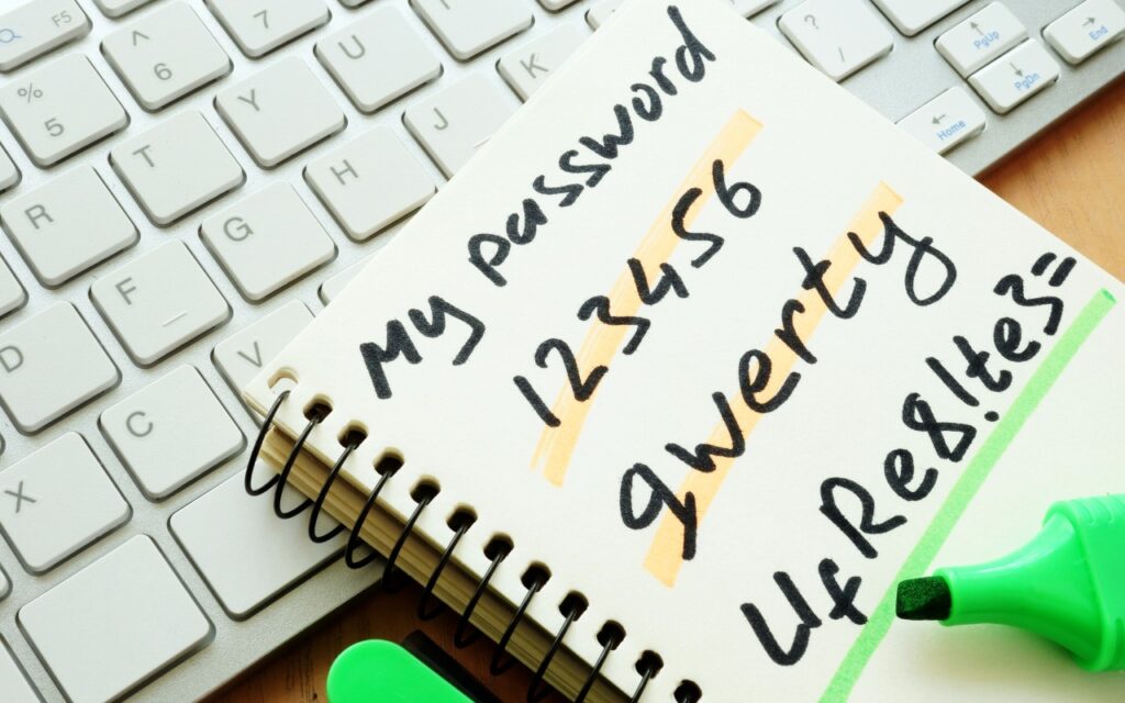 A notebook with My password written on it lists weak passwords—123456, qwerty, and UfRe8!te3=—next to a keyboard and a green highlighter, hinting at the new Passwords app in macOS 15 Sequoia, iOS 18, and iPadOS 18.