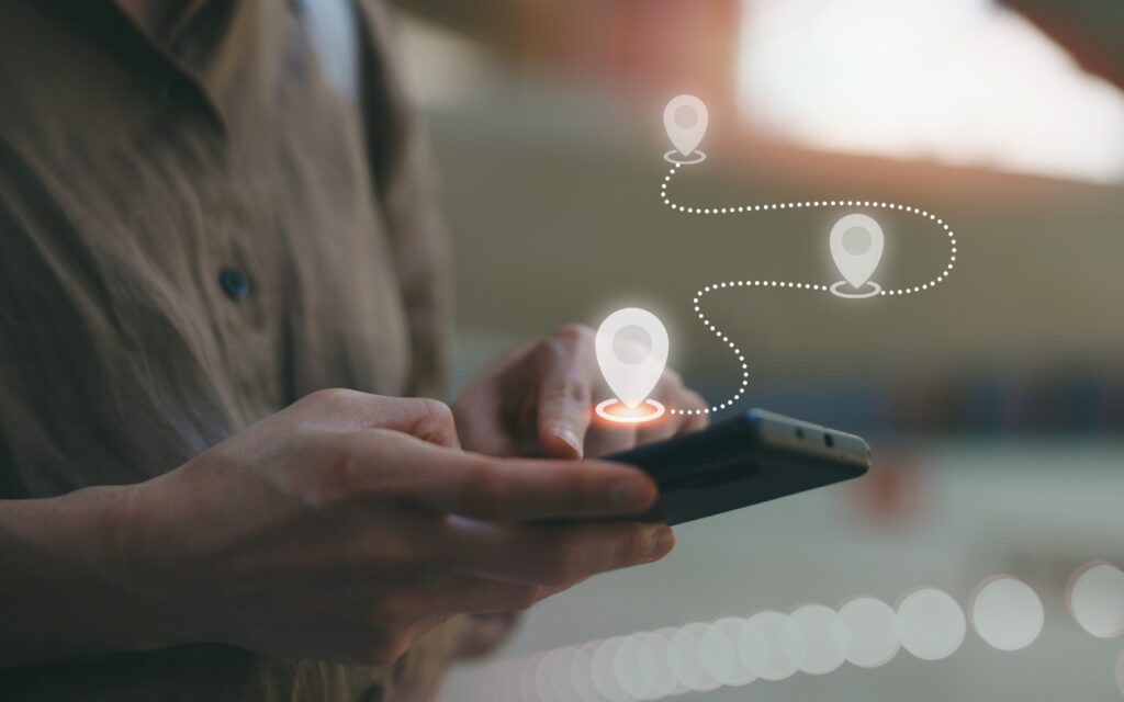 Perturbed by Location Tracking Revelations? Here’s How to Protect Yourself: A person uses a smartphone, with digital map location pins and a dotted path overlaid, representing navigation or GPS tracking technology.