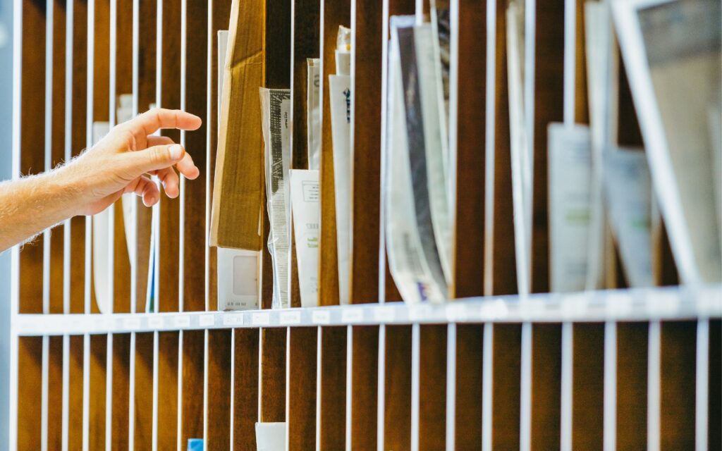 A hand reaches toward a mail slot in a wooden mail sorting wall filled with envelopes, packages, and documents organized into compartments—much like how Mail on the iPhone can categorize your messages in iOS 18.2.