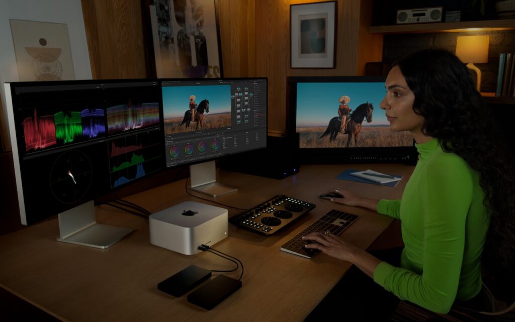 A person in a green shirt edits a photo of someone on horseback using two large monitors, color grading equipment, and a Mac Mini in a modern workspace with wooden decor—where Apple updates Mac Studio with M4 Max and M3 Ultra chips.