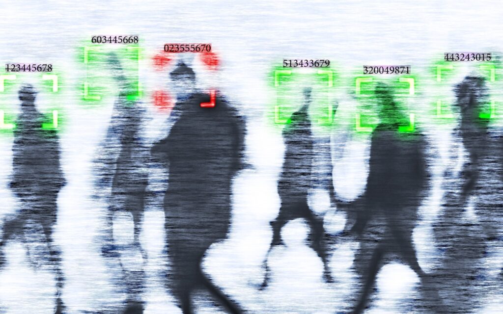 A blurred image of people walking, with digital square overlays around their faces and numbers above their heads, simulating facial recognition technology. In times of uncertainty, increase your digital privacy and security as two faces are highlighted in red, others in green.