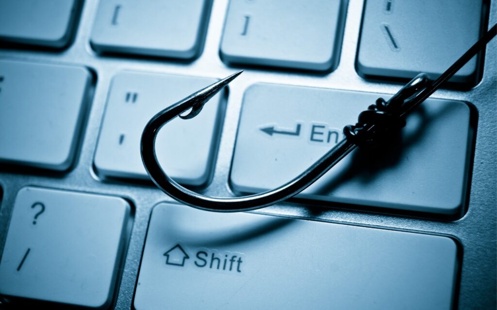 A fishing hook placed on a computer keyboard, symbolizing online phishing scams or cyber security threats. The hook rests near the Enter key—beware domain name renewal phishing attacks targeting unsuspecting users.