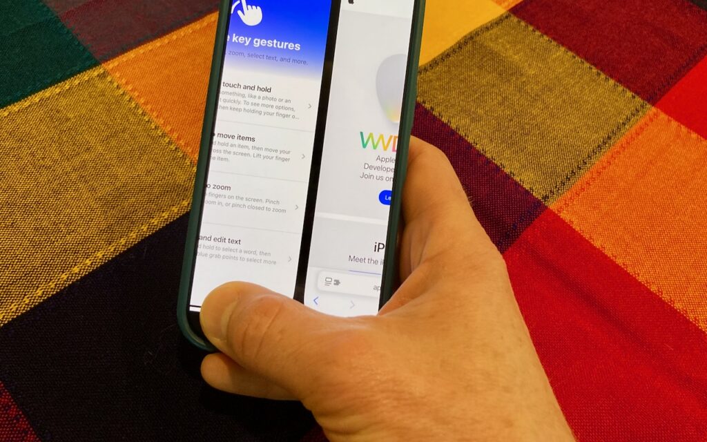 A hand holds a smartphone displaying two apps side by side on a colorful plaid tablecloth, highlighting split-screen multitasking and how you can switch between apps fluidly on Face ID iPhones.